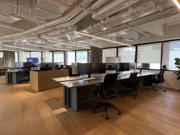 משרד מודרני בעל חלל פתוח להשכרה במידטאון, מנחם בגין; כולל שולחנות עבודה מרובים, מסכי מחשב, כיסאות משרדיים, חלונות גדולים וצינורות תקרה חשופים — אור טבעי ממלא את חלל העבודה המסוגנן.
