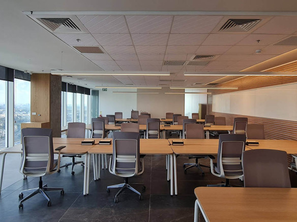 משרד להשכרה במגדל סקיי, הכולל שורות של שולחנות וכסאות ריקים, חלונות גדולים עם נוף לעיר, לוח לבן על קיר אחד, והתקנת פלאג אנד פליי לשימוש מיידי.