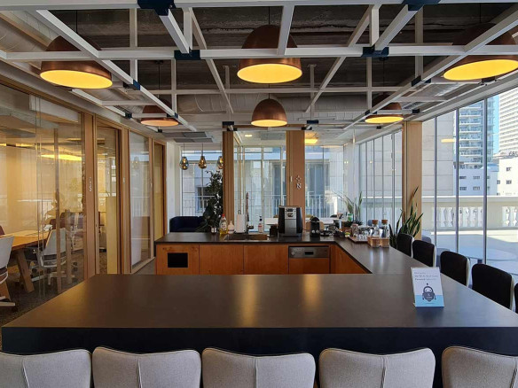 מטבח משרדי מודרני עם אי מרכזי, מכונת קפה, תאורה תקרתית וקירות זכוכית המשקיפים על העיר – חלל מושלם במשרד להשכרה בשדרות רוטשילד, תל אביב.