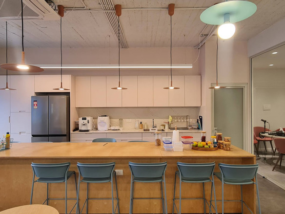 מטבח משרדי מודרני במשרד להשכרה בתל אביב, הכולל אי מעץ, כסאות בר בצבע טורקיז, מכשירי חשמל אלגנטיים, תאורה תלויה וחדר ישיבות עם קירות זכוכית — המשתרע על פני 200 מ"ר של חלל עבודה מסוגנן.