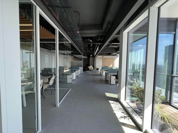 משרד להשכרה מודרני בחסן ערפה עם קירות זכוכית, עמדות עבודה וחלונות גדולים המאפשרים כניסת אור טבעי; כולל תצורת פלאג אנד פליי עם צמחייה ונוף לעיר.