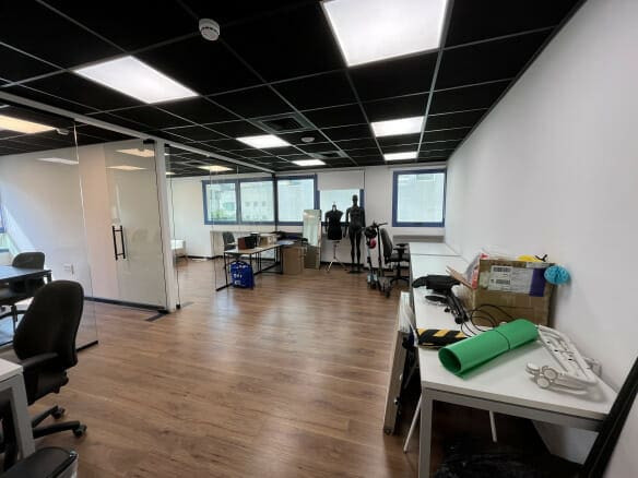 חלל משרדי מודרני עם שולחנות, כיסאות, בובות תצוגה וציוד מגוון על השולחנות; חדר ישיבות עם קירות זכוכית וחלונות גדולים נראים לעין.