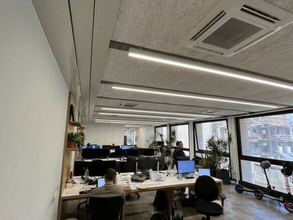 משרד פתוח עם מספר שולחנות, מחשבים ואנשים עובדים; חלונות גדולים משקיפים על אתר בנייה בחוץ; קטנועים חשמליים חונים ליד החלון.