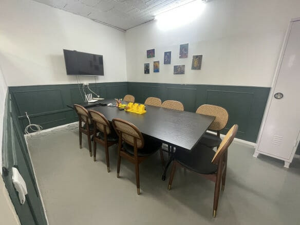 חדר ישיבות עם שולחן מלבני, שמונה כיסאות, טלוויזיה על הקיר, כמה תמונות ממוסגרות ופריט דקורטיבי צהוב על השולחן.