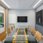 חדר ישיבות מודרני עם שולחן זכוכית, שמונה כיסאות עץ, טלוויזיה המותקנת על הקיר, לוח לבן ויצירות אמנות בנושא ספורט על קירות אפורים.