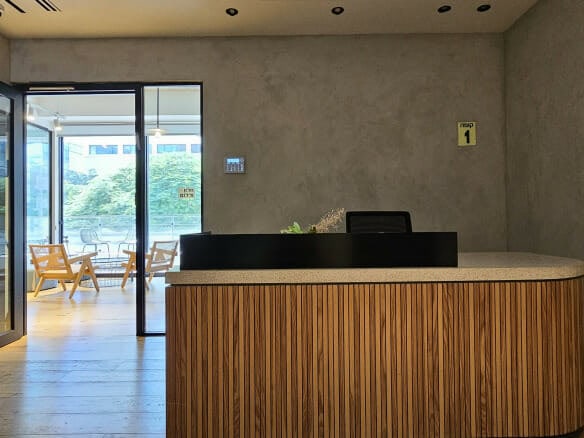 דלפק קבלה מודרני בלובי משרד מינימליסטי עם דלת זכוכית פתוחה המובילה לאזור ישיבה וחלונות גדולים.