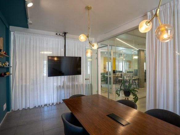 חדר ישיבות מודרני עם שולחן עץ, ארבעה כיסאות, תאורת תקרה, טלוויזיה המותקנת על הקיר, וילונות לבנים וקירות זכוכית המשקיפים על חלל משרדי במשרד להשכרה בהר סיני בלב מרכז תל אביב.