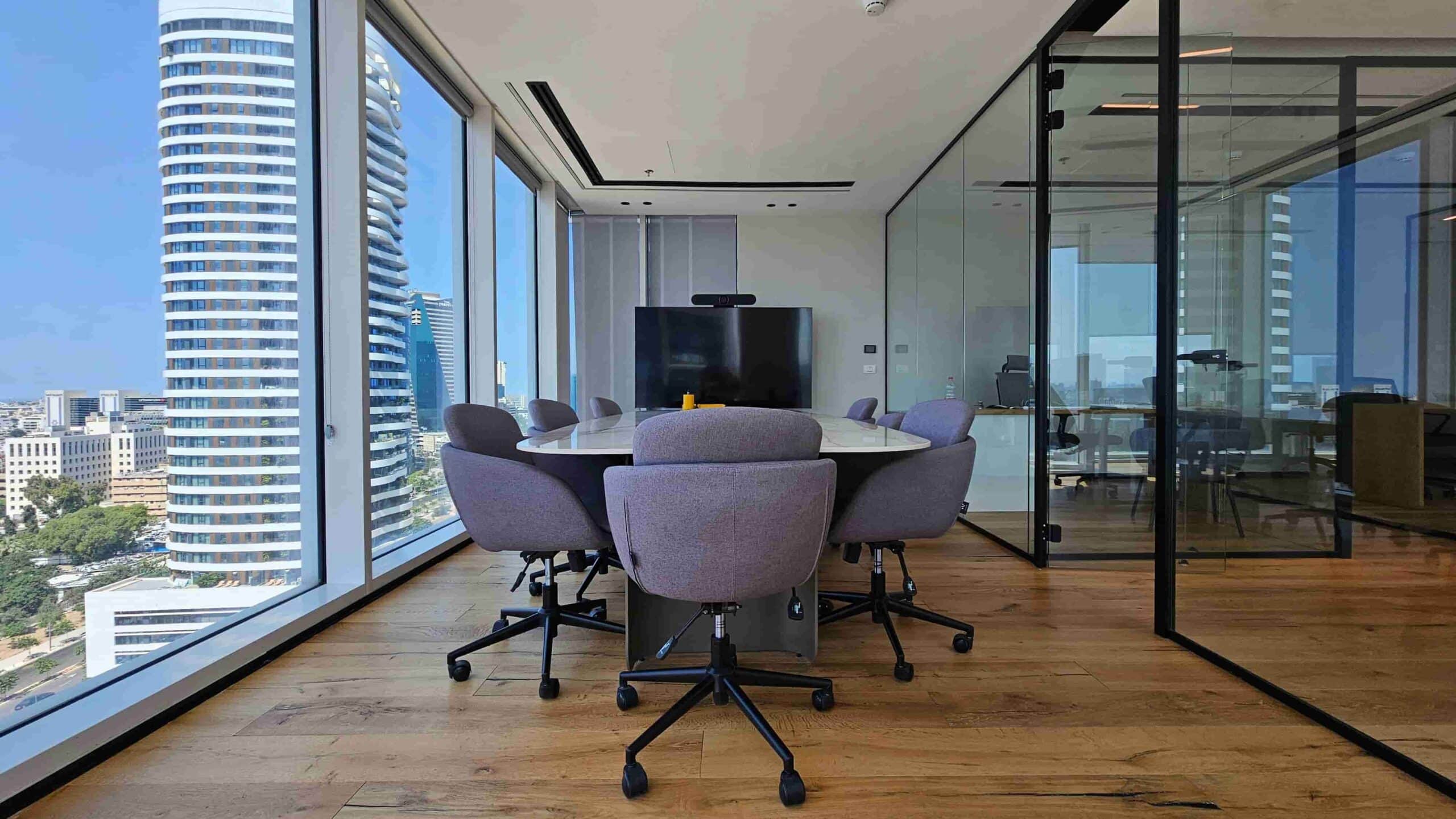 חדר ישיבות מודרני עם שולחן עגול, שישה כיסאות אפורים, חלונות גדולים המשקיפים על בנייני העיר במגדל SKY, וקירות זכוכית המפרידים בין המשרד במגדל לשאר חלל המשרדים. חדר ישיבות מודרני עם שולחן עגול, שישה כיסאות אפורים, חלונות גדולים המשקיפים על בנייני העיר במגדל SKY, וקירות זכוכית המפרידים בין המשרד במגדל לשאר חלל המשרדים.