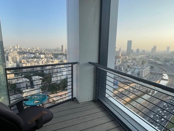 מרפסת קטנה עם כיסא ושולחן צד, המשקיפה אל נוף עירוני שוקק עם מגדל רסיטל, גורדי שחקים וכביש מהיר עמוס תנועה.