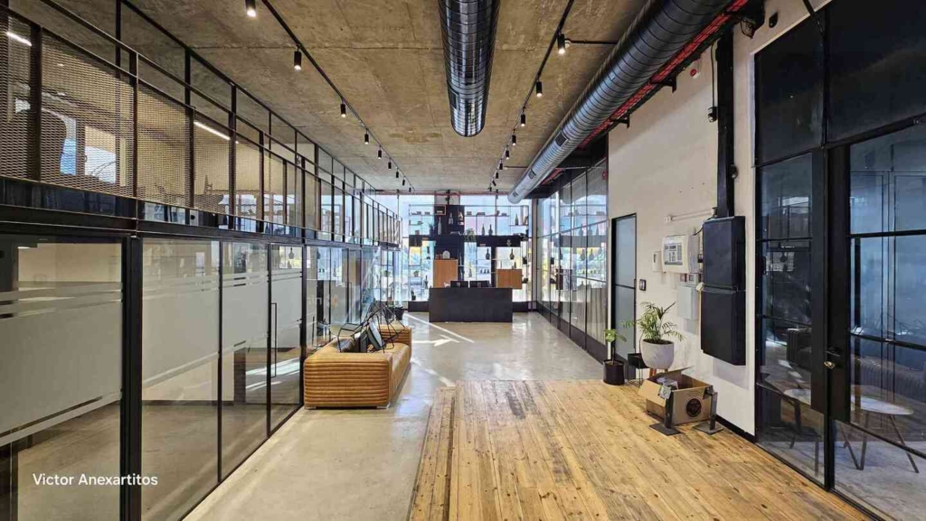 משרד מודרני בעל חלל פתוח ברחוב אחים מסלאויטה 11, עם חדרי ישיבות בעלי קירות זכוכית, תקרות תעשייתיות, רצפות עץ, פינות ישיבה וצמחים בעציצים, המוארים על ידי חלונות גדולים ותאורה תקרתית.