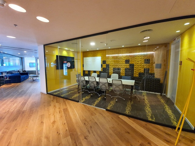 חדר ישיבות מודרני עם קירות צהובים, שולחן ארוך, מספר כיסאות משרדיים וקירות זכוכית במשרד להשכרה במגדל עזריאלי תל אביב, הסמוך למרחב עבודה פתוח עם ריצוף עץ.