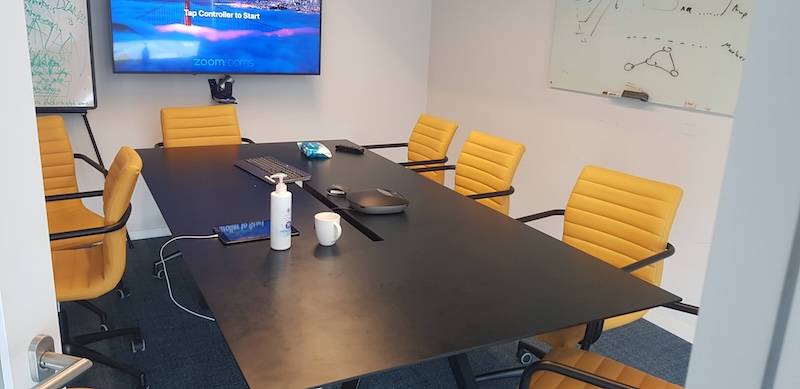 חדר ישיבות במגדלי הארבעה ליד שרונה, הכולל שולחן שחור, שישה כיסאות צהובים, לוח לבן, מסך זום ופריטים חיוניים כמו מקלדת, חומר חיטוי, כוס קפה וחטיפים – מושלם לצרכי המשרד שלכם בשטח של 800 מ"ר.