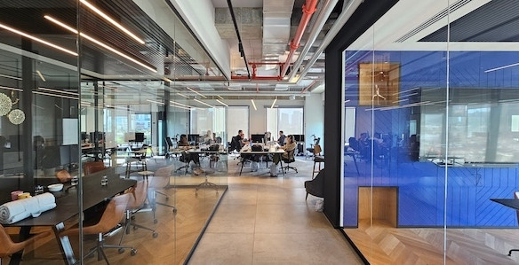 חלל משרדים מודרני בעל תכנון פתוח, בו עובדים מספר אנשים ליד שולחנות במגדל רסיטל; קירות זכוכית מחלקים את אזורי הישיבות והפגישות, ומציעים אפשרויות השכרה בתל אביב עם משרד עם מרפסת לנוחות נוספת.