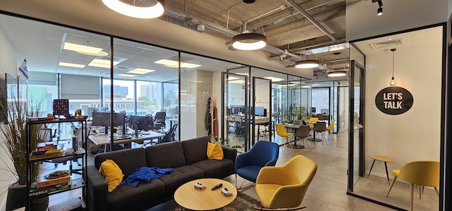 שטחי משרדים מודרניים להשכרה במגדלי הארבעה, תל אביב, הכוללים חדרי ישיבות עם קירות זכוכית, שולחנות מחשב, טרקלין נעים עם ספות וכסאות, ושלט "Let's Talk" על חדר ישיבות פרטי.