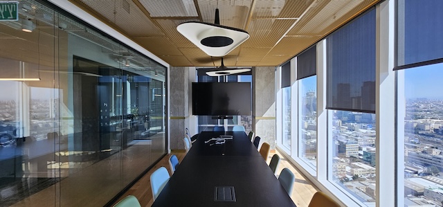 חדר ישיבות מודרני להשכרה במגדל סקיי, הכולל שולחן ארוך, כיסאות רבים, חלונות גדולים עם נוף לעיר, טלוויזיה המותקנת על הקיר ותאורת תקרה — משרד מרוהט אידיאלי המוכן לצרכי העסק שלכם.