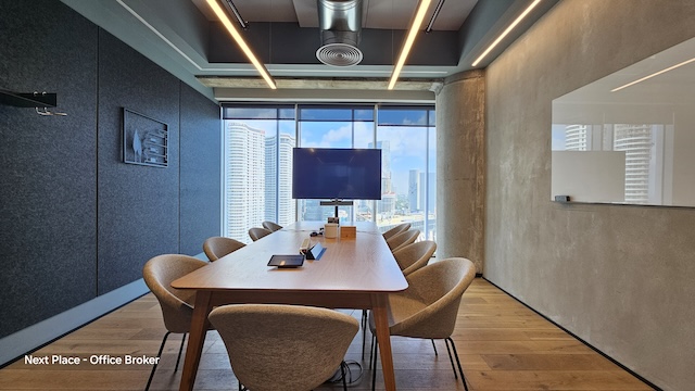 חדר ישיבות מודרני עם שולחן עץ, שישה כיסאות, מסך קיר וחלונות גדולים המשקיפים על בנייני העיר במגדל אקרו — מושלם לישיבות בדירה להשכרה בתל אביב עם עיצוב מינימליסטי.