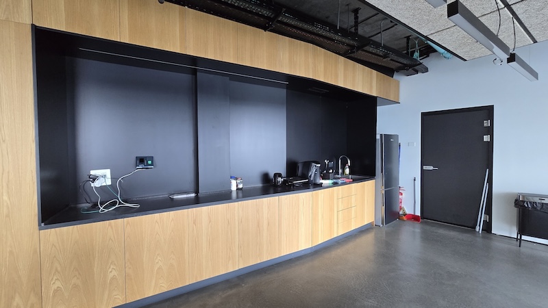 מטבחון מודרני ומרוהט עם ארונות עץ, משטח עבודה שחור, כיור, מכשירי חשמל ומקרר קטן על רקע קיר כהה במגדל ספיר.