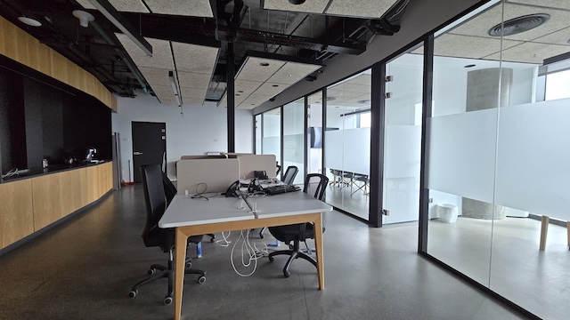 משרד מרוהט ומודרני במגדל ספיר עם מספר שולחנות וכסאות, ציוד מחשב, חדרי ישיבות עם קירות זכוכית ותאורה טבעית מינימלית ליד הבורסה.