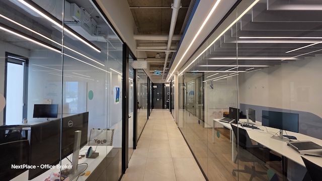מסדרון משרדים מודרני במגדל רסיטל, הכולל חללי עבודה עם קירות זכוכית ושולחנות עם מחשבים על רצפת אריחים מלוטשת תחת תאורה תקרתית בהירה — משרד מרוהט מושלם בקומה להשכרה.