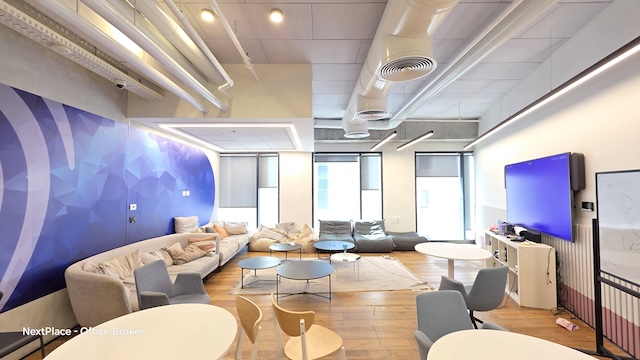 לשכור סלון משרדי מודרני במגדל רסיטל עם ספות, כורסאות, שולחנות עגולים, מסך גדול על הקיר ואומנות גאומטרית. חלל מואר עם רצפת עץ ותקרה חשופה בקומה עצמאית.