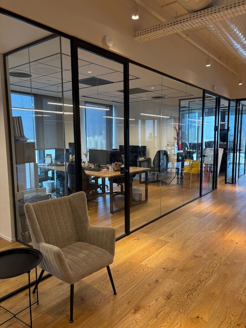 שטחי משרדים מודרניים להשכרה בתל אביב, הכוללים חדרי ישיבות עם קירות זכוכית, עמדות עבודה עם מחשבים, כורסה אפורה במסדרון וריצוף עץ מסוגנן במגדל רסיטל.