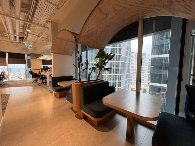 אזור ישיבה מודרני עם ספות, צמחים פנימיים וחלונות גדולים המשקיפים על נוף העיר תל אביב – מושלם למשרד מרוהט ומעורר השראה במגדלי סקיי.