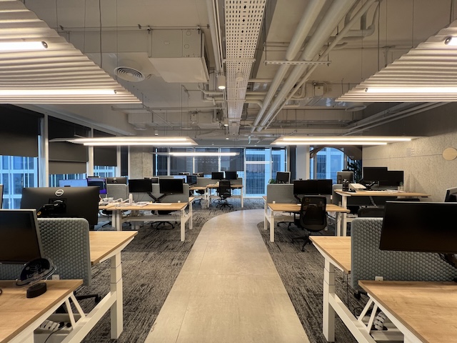 משרד מודרני בעל חלל פתוח עם שורות של שולחנות, מחשבים וכסאות, המואר בתאורת תקרה; חלונות גדולים משתרעים לאורך הקיר הרחוק במשרד מרוהט במגדלי סקיי, תל אביב.