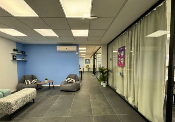 משרד מרוהט ומודרני ברחוב המסגר, תל אביב, עם קיר דקורטיבי כחול, שני פופים, ספסל ומסדרון המוביל לחדרי ישיבות עם קירות זכוכית.