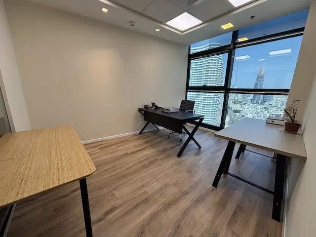 משרד להשכרה מודרני עם ריצוף עץ, שלושה שולחנות, טלפון ומחשב נייד בבית רובינשטיין, תל אביב, עם חלון גדול המשקיף על נוף עירוני עם בניינים גבוהים.