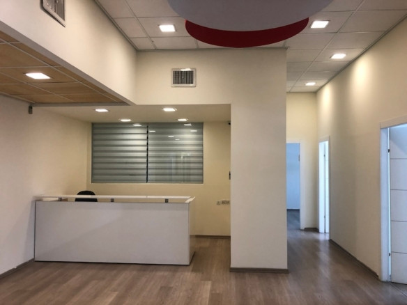 אזור קבלה מודרני וריק עם שולחן לבן, חלון זכוכית, קירות בצבע בז', ריצוף עץ ותאורה תקרתית בבית הקרן, מתחם הבורסה – משרד להשכרה המתאים לעסקים.