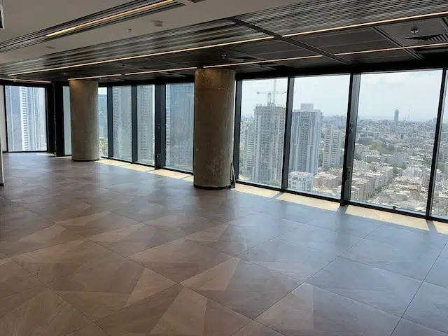 משרד להשכרה במגדל רסיטל תל אביב, עם חלונות ענק מהרצפה עד התקרה, נוף עירוני מרהיב, רצפת אריחים ועמודים חשופים.