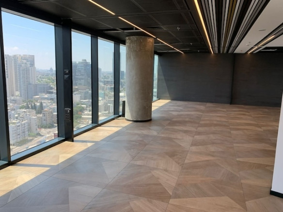 משרד להשכרה ריק ומודרני במגדל רסיטל, תל אביב, עם חלונות גדולים מהרצפה עד התקרה, ריצוף אריחים בדוגמת עץ, עמוד בטון ונוף עירוני מרהיב.