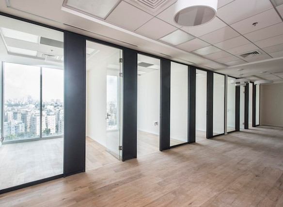 משרד מודרני וריק בתל אביב עם חדרים פרטיים בעלי קירות זכוכית, ריצוף עץ, קירות לבנים וחלונות גדולים המשקיפים על העיר, הממוקם במגדל WE — משרד להשכרה אידיאלי.