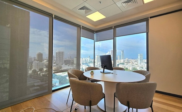 משרד להשכרה במגדל רסיטל, הכולל חדר ישיבות עם ארבעה כיסאות סביב שולחן עגול, צג על השולחן וחלונות גדולים המשקיפים על קו הרקיע המרהיב של העיר.