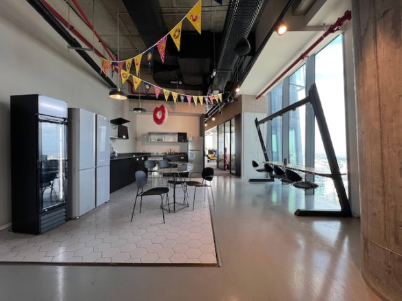 מטבחון מרוהט ומודרני עם פינת אוכל, דגלונים חגיגיים, מקררים ונדנדה ליד חלונות מהרצפה לתקרה המשקיפים על העיר בעזריאלי שרונה.