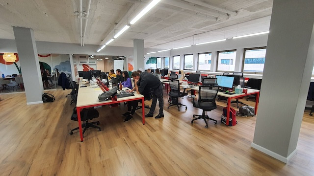 משרד להשכרה ברחוב החשמונאים, עם אנשים עובדים על מחשבים, רצפות עץ, חלונות גדולים המחדירים אור טבעי ומרפסת נעימה.
