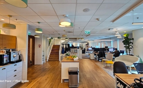 משרד מודרני בעל חלל פתוח להשכרה במגדל סונול, הכולל משרד מרוהט עם שולחנות, מחשבים, פינת ישיבה, מטבחון בצד שמאל ומדרגות מרכזיות המובילות לקומה העליונה. מספר אנשים עובדים בנוחות ליד שולחנותיהם.