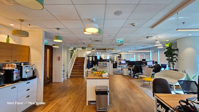 משרד מודרני בעל חלל פתוח להשכרה במגדל סונול, הכולל משרד מרוהט עם שולחנות, מחשבים, פינת ישיבה, מטבחון בצד שמאל ומדרגות מרכזיות המובילות לקומה העליונה. מספר אנשים עובדים בנוחות ליד שולחנותיהם.