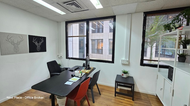 משרד קטן להשכרה עם שולחן, מחשב, כיסא ותמונות של ראשי איילים על הקירות. חלונות גדולים מכניסים אור טבעי. יש מדף לבן, עציץ בפינה וגישה למרפסת להפסקה.