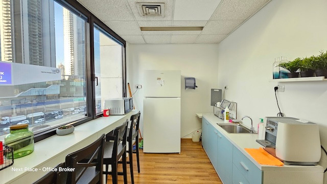 מטבח קטן במשרד עם מקרר, כיור, מכונת קפה, דלפק ישיבה ליד חלון וצמחים ירוקים על מדף. תוכלו ליהנות מנוף של בניינים גבוהים ומגישה נוחה למרפסת במשרד להשכרה בבית אגיש רבד.