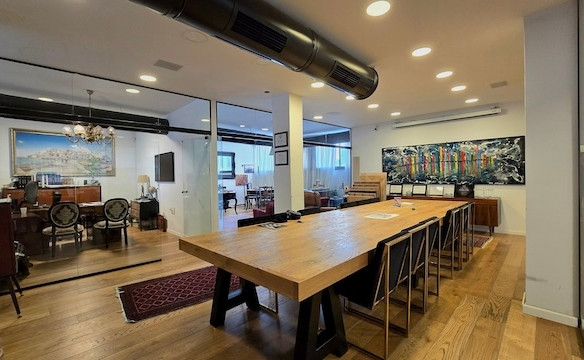 חלל משרדי מודרני להשכרת קומה בשכונת מונטיפיורי, הכולל שולחן ישיבות עץ ארוך, כיסאות שחורים, מחיצות זכוכית, רצפות עץ מלא וציורים צבעוניים על הקירות.