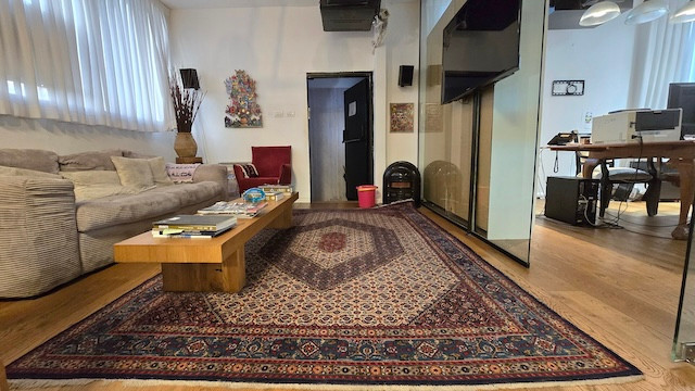 סלון עם שטיח מעוצב, שולחן קפה מעץ, ספה בצבע בז', אמנות קיר ופינת עבודה צמודה — אידיאלי קומה להשכרה בשכונת מונטיפיורי, במיקומו המרכזי על מנחם בגין.