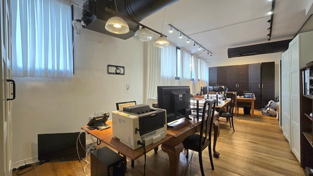 משרד מודרני להשכרה ברחוב מנחם בגין, הכולל רצפות עץ, שולחנות עבודה מרובים עם מחשבים ומדפסות, ארונות מרווחים בחלק האחורי וחלונות עם תריסים אנכיים המאפשרים כניסת אור טבעי.