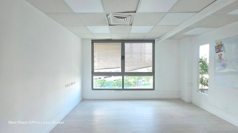 חדר משרדי ריק עם קירות לבנים, רצפת עץ בהירה וחלונות גדולים עם תריסים; ניתן לראות חלק מתרשים קיר בצד ימין. ממוקם בקומה 4 בבניין על מנחם בגין, בשטח של כ-300 מטר.