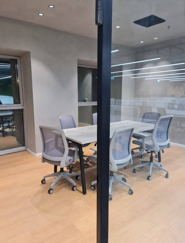 חדר ישיבות קטן ומודרני עם שולחן מלבני וחמש כיסאות משרדיים על גלגלים, הנשקף מבעד לקיר זכוכית במגדל רוגובין תדהר, בורסה רמת גן.