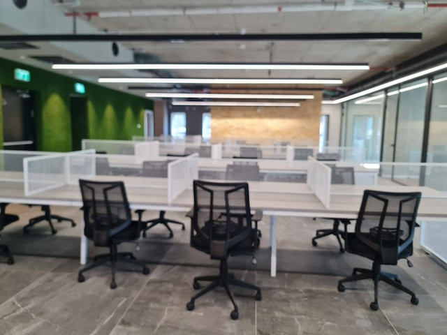 משרד מרוהט מודרני בעל חלל פתוח עם שולחנות ריקים, כיסאות שחורים, מחיצות ותאורה תקרתית. החלל כולל קירות זכוכית, קיר ירוק בולט והתקנת plug&play נוחה במגדל רוגובין תדהר.