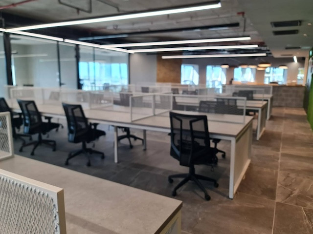 משרד מודרני וריק בתכנון פתוח במגדל רוגובין תדהר, בורסה רמת גן, עם שורות של שולחנות וכסאות משרדיים שחורים תחת תאורה חזקה, מציג משרד מרוהט ומרווח.