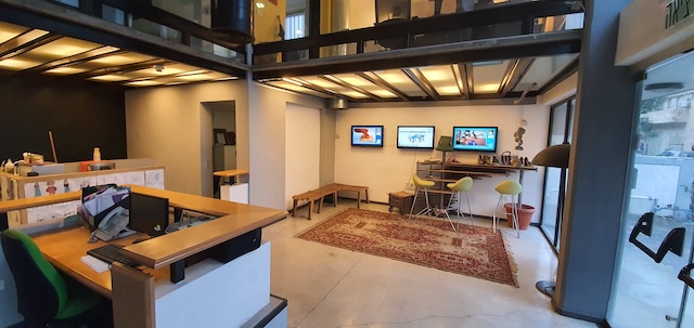 עיצוב פנים מודרני למשרד בבניין עצמאי להשכרה במונטיפיורי, 350 מ"ר עם שולחנות, מחשבים, פינת ישיבה עם שלושה כיסאות, שטיח ושלושה מסכים על הקיר. חלונות גדולים מציפים את החלל באור טבעי.