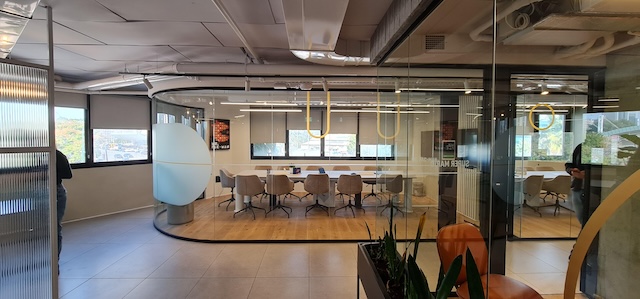 משרד מרוהט ומודרני עם חדר ישיבות בעל קירות זכוכית, שולחן ארוך, כיסאות, חלונות גדולים וצמחים דקורטיביים, הממוקם ברחוב דרך השלום בתל אביב. כולל גישה למרפסת גג מרווחת בגודל 600 מ"ר.