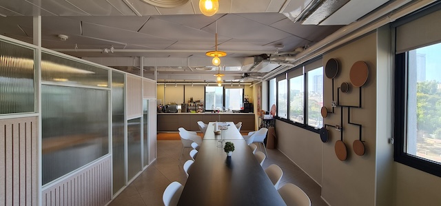 מטבח ומטבח מודרני עם שולחן שחור ארוך, כיסאות לבנים, חלונות גדולים וקישוטים על הקירות, מואר בתאורת תקרה - ממוקם על גג 600 מ"ר משרד מרוהט בדרך השלום תל אביב.